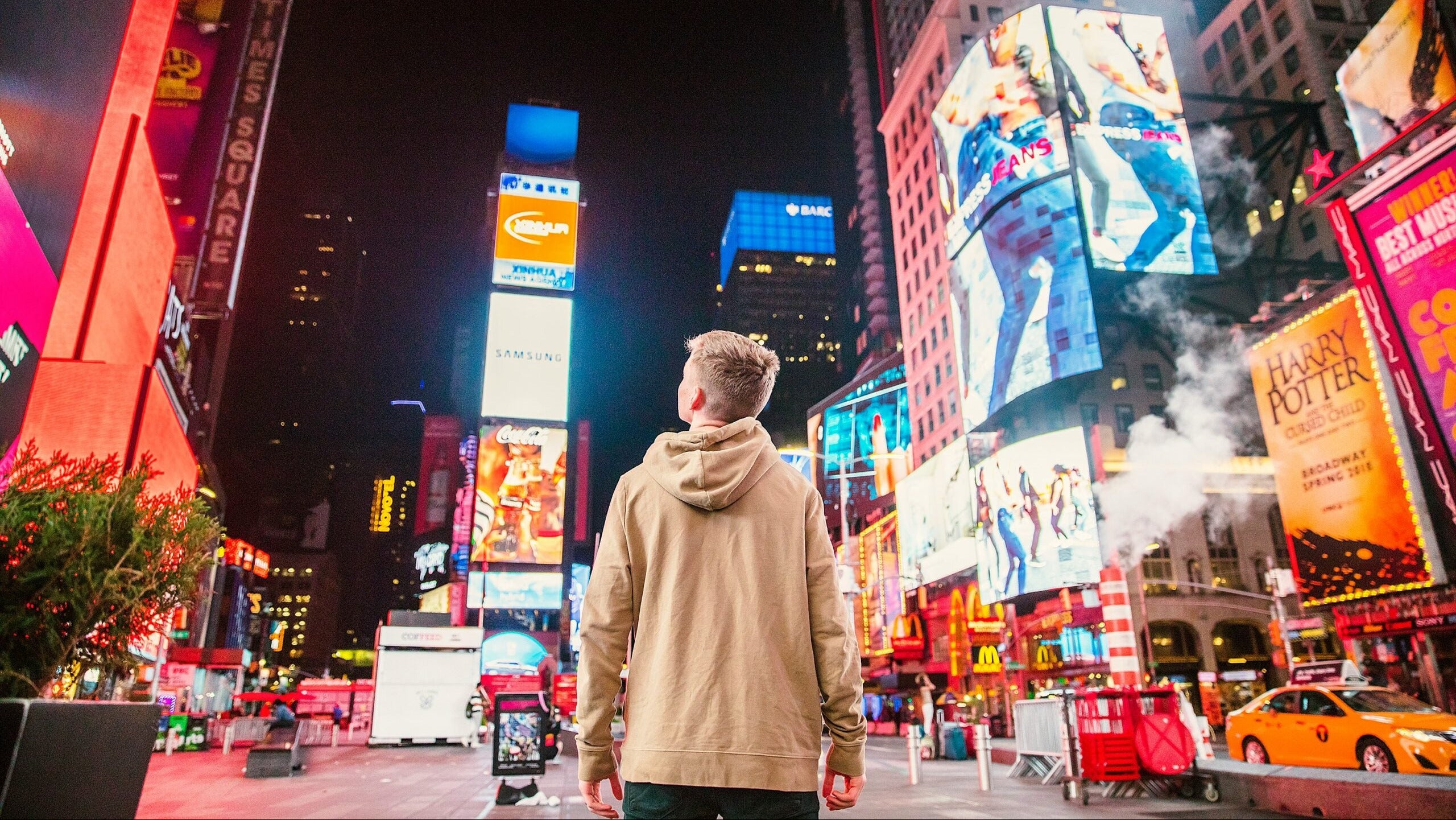 Man standing in a bustling city street at night with illuminated billboards and advertisements.